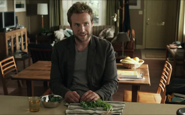 HD PC desktop wallpaper (movie: Life of Pi) — a man chops herbs at a kitchen table, warm light and a cozy, lived-in living room visible behind him.