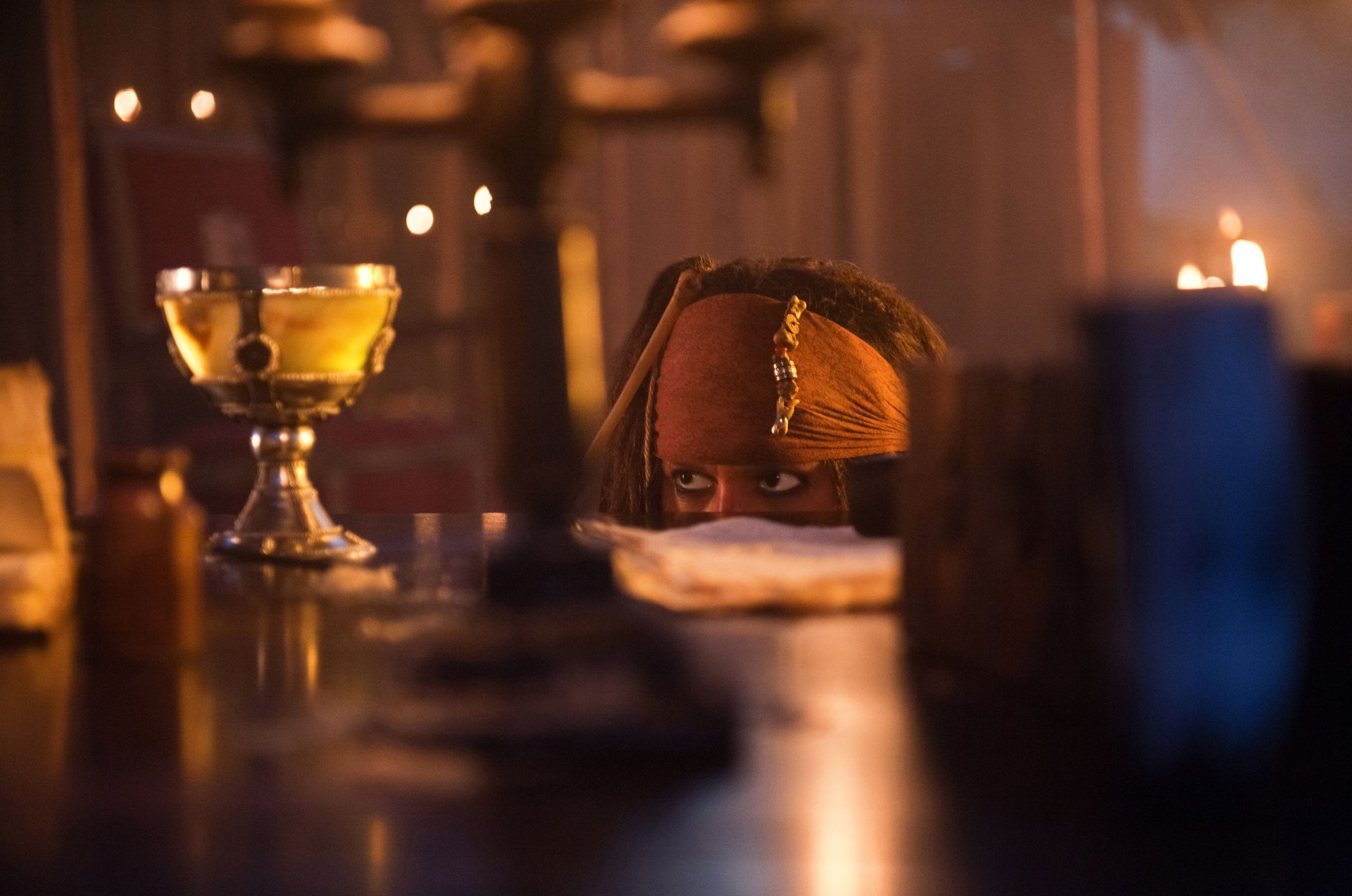 Jack Sparrow, played by Johnny Depp in Pirates of the Caribbean: On Stranger Tides, peeks over a table in a dimly lit 4K Ultra HD movie scene.