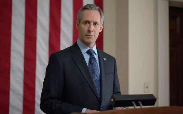A confident character stands in front of a large American flag, embodying the political intrigue of the TV show *House of Cards*. This HD desktop wallpaper captures a powerful moment.