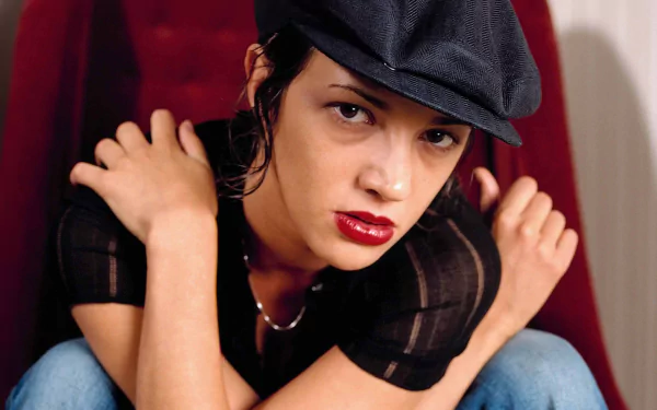 A striking HD wallpaper featuring Italian actress Asia Argento, showcasing her edgy style with a cap, bold lipstick, and a captivating pose against a vibrant background.
