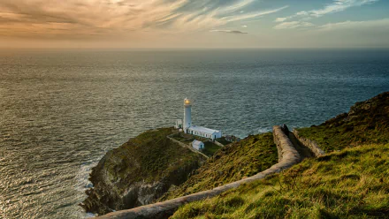 A stunning 4K Ultra HD image of a lighthouse on a cliff in Santorini, overlooking the tranquil sea, bathed in warm light during sunset, showcasing man-made beauty in nature.