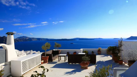 Sunlit terrace with white architecture overlooking the deep blue Aegean Sea on Santorini, Greece, captured in stunning 4K Ultra HD resolution.