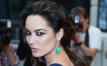 HD desktop wallpaper featuring French actress Bérénice Marlohe in a close-up portrait with dramatic makeup and turquoise earrings.