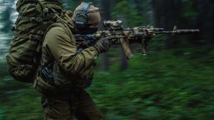 A Russian Spetsnaz soldier in tactical gear and a backpack aims his firearm in a dense forest, captured in action for an HD desktop wallpaper and background.