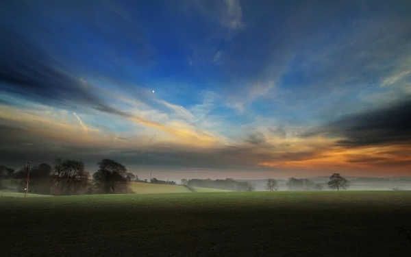 HD desktop wallpaper of a scenic landscape featuring a foggy field at dawn with vibrant skies and silhouetted trees.