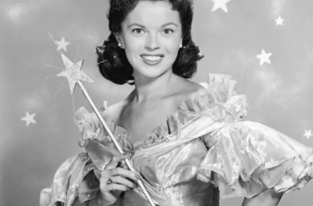 Black and white HD desktop wallpaper featuring celebrity Shirley Temple smiling, dressed in a ruffled gown and holding a star-tipped wand against a starry background.