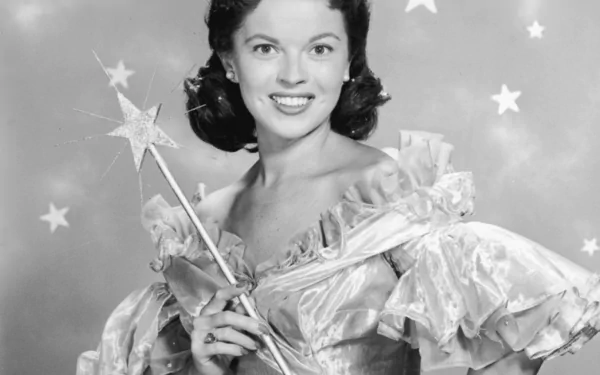 Black and white HD desktop wallpaper featuring celebrity Shirley Temple smiling, dressed in a ruffled gown and holding a star-tipped wand against a starry background.