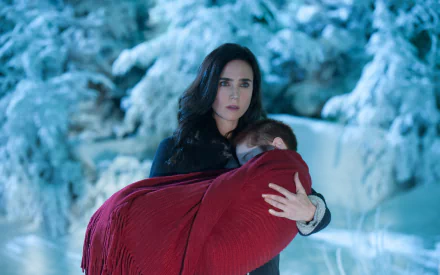 Virginia Gamely holds a child wrapped in a red blanket against a snowy backdrop in this captivating scene from the movie *Winter's Tale*, featuring Jennifer Connelly.