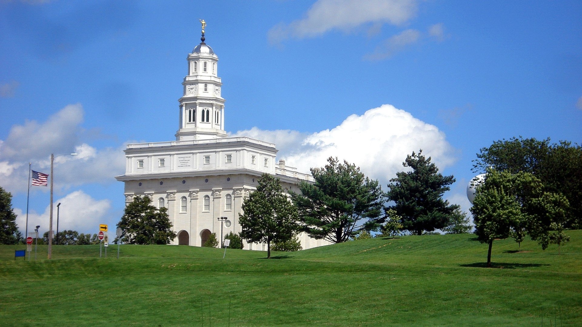 HD PC desktop wallpaper featuring the white Nauvoo Temple under a bright blue sky with green grass and trees in the foreground, highlighting its religious significance.