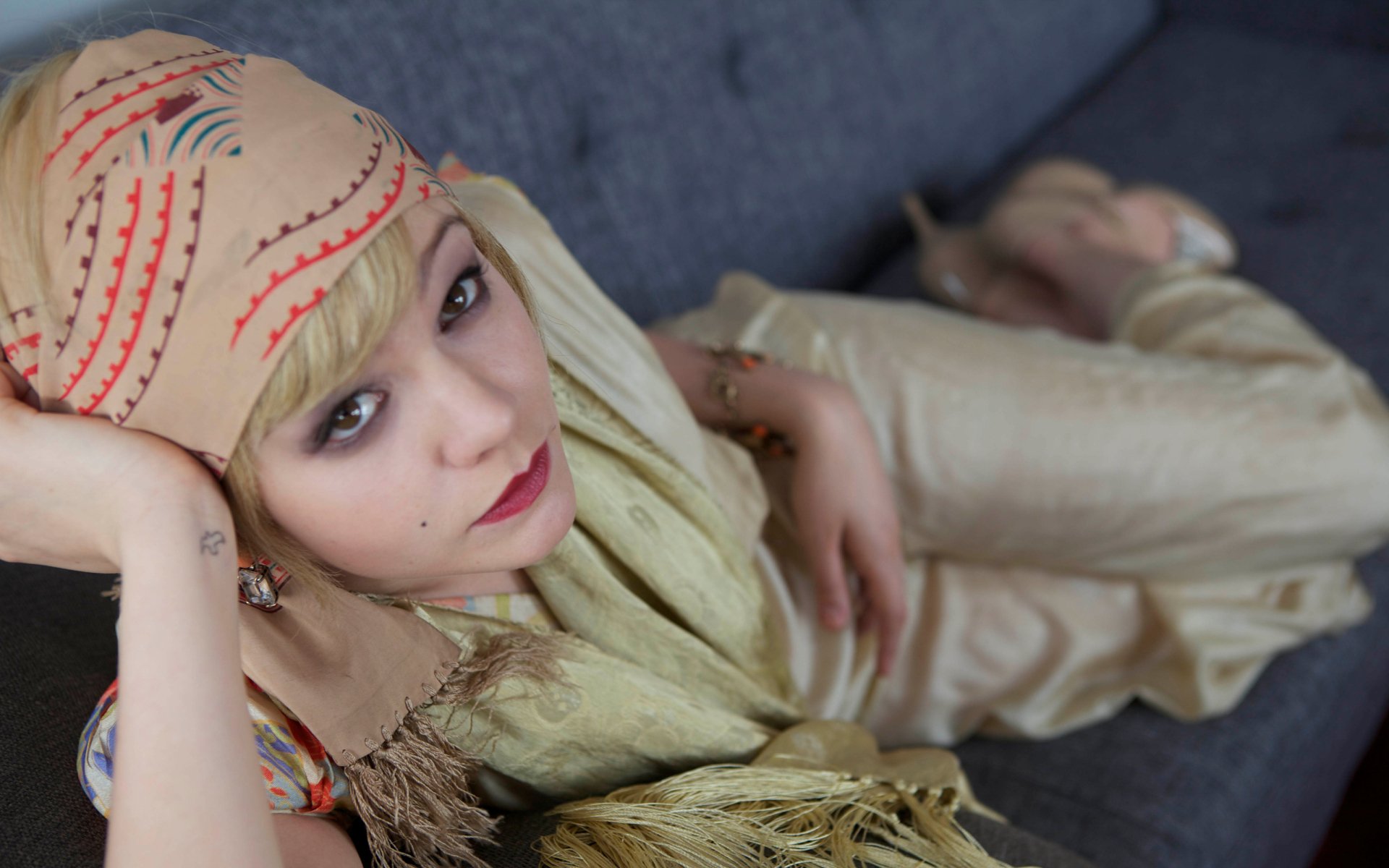 HD desktop wallpaper featuring actress Carey Mulligan in costume from the movie The Great Gatsby, posed reclining on a dark sofa with a vintage headscarf and elegant attire.
