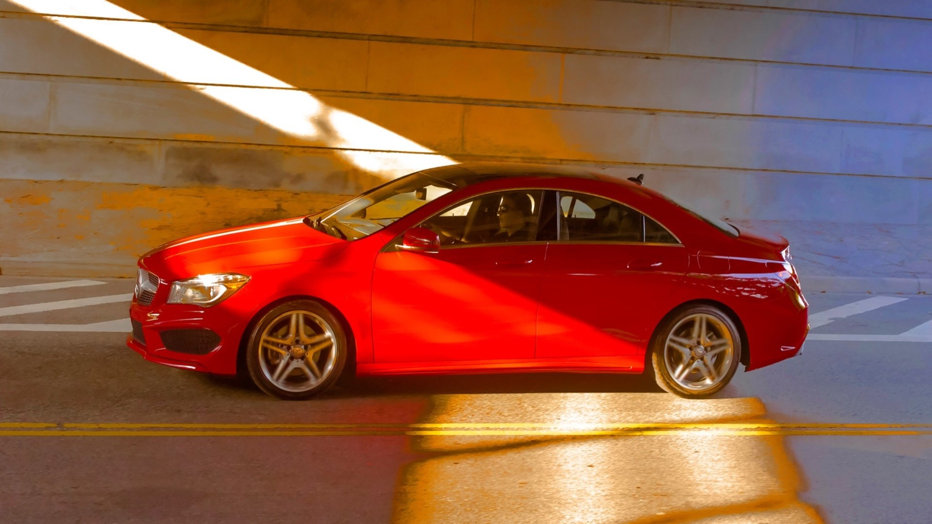 HD PC desktop wallpaper featuring a red Mercedes-Benz CLA-Class parked indoors with warm sunlight casting dramatic shadows on the vehicle and surrounding walls.