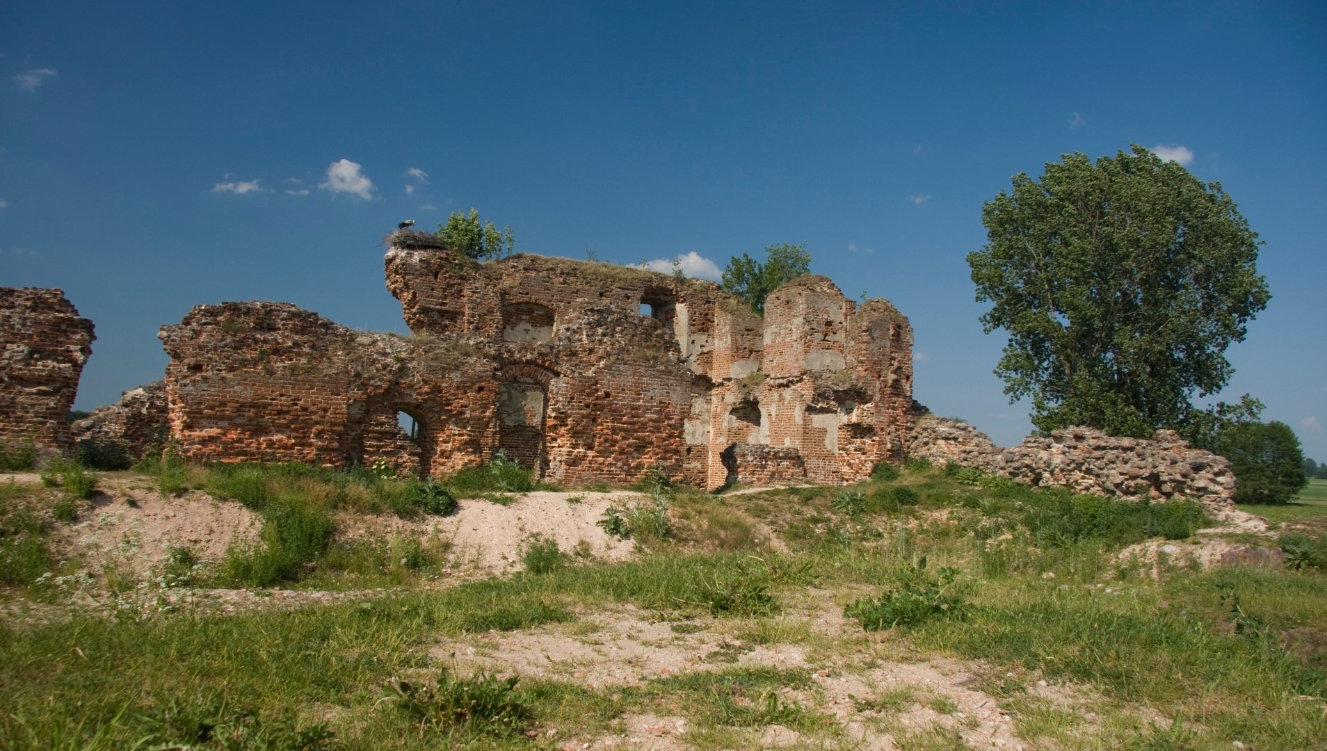 HD PC desktop wallpaper of Besiekiery Castle ruins — man-made stone walls on a grassy hill beneath a clear blue sky.