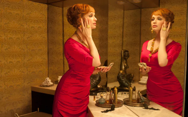HD PC desktop wallpaper featuring American actress Christina Hendricks in a red dress, standing thoughtfully by a mirror in a vintage-style bathroom.