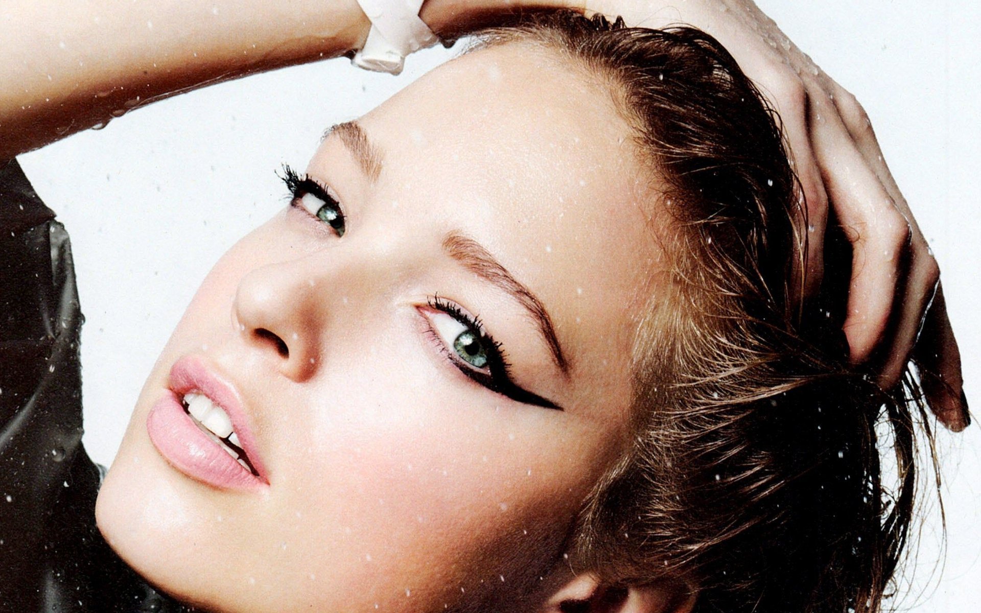 Close-up HD desktop wallpaper of a French model woman with dramatic winged eyeliner, glossy lips, hand in hair and head tilted back.