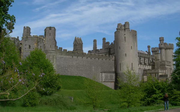 HD desktop wallpaper of the man-made Arundel Castle set against a partly cloudy blue sky and surrounded by lush greenery.