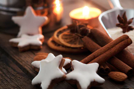 A close-up 4K Ultra HD PC desktop wallpaper featuring star-shaped iced cookies, cinnamon sticks, almonds, and warm candlelight on a rustic wooden surface.