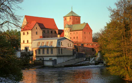 HD desktop wallpaper featuring the man-made Castle of Pomeranian Dukes by a river, surrounded by autumn trees under a clear sky.