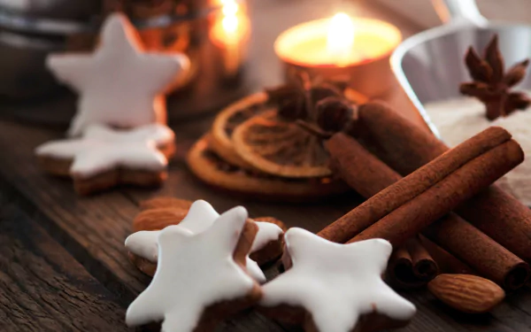 A close-up 4K Ultra HD PC desktop wallpaper featuring star-shaped iced cookies, cinnamon sticks, almonds, and warm candlelight on a rustic wooden surface.