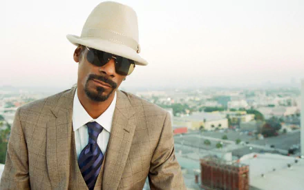 Music-themed HD PC desktop wallpaper: a stylish man in a tan suit, white fedora and sunglasses posing against a soft-focus city skyline background.