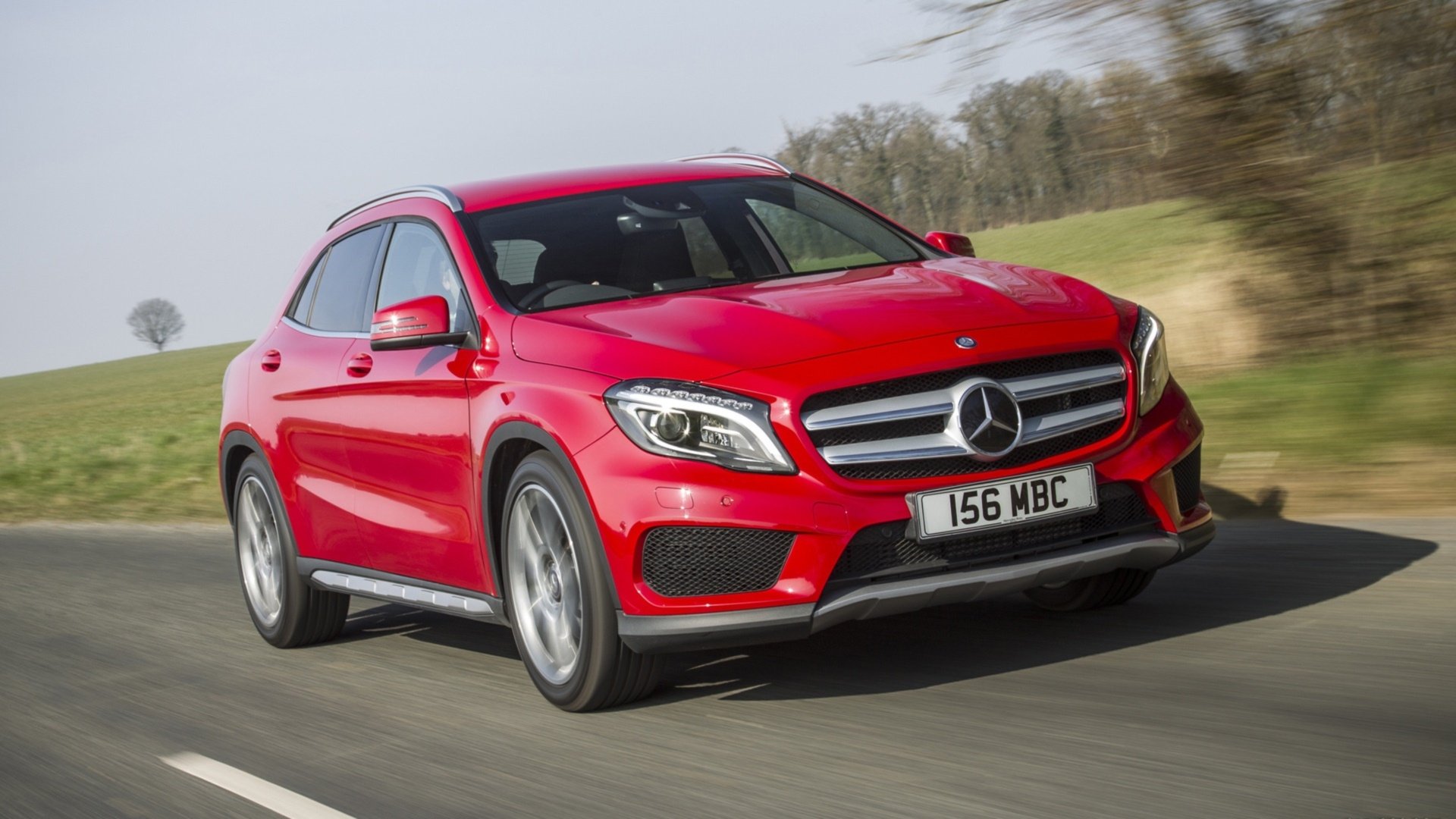 HD desktop wallpaper featuring a red Mercedes-Benz GLA-Class vehicle driving on a countryside road.
