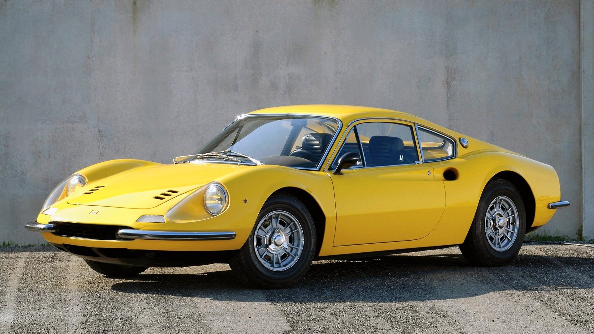 HD desktop wallpaper featuring a yellow Ferrari Dino 206 GT parked against a plain concrete wall, showcasing its classic sports car design.