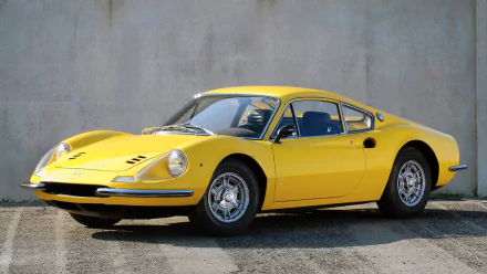 HD desktop wallpaper featuring a yellow Ferrari Dino 206 GT parked against a plain concrete wall, showcasing its classic sports car design.