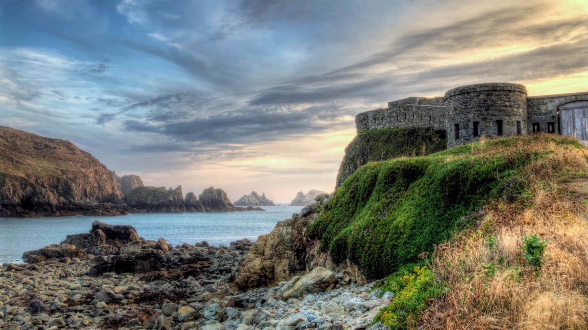 A stunning HD desktop wallpaper featuring Fort Clonque, showcasing its historic stone structure against a dramatic coastal landscape and serene sky.