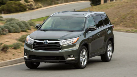 HD desktop wallpaper showing a dark gray Toyota Highlander Hybrid SUV driving on a curved road with greenery in the background.