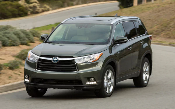 HD desktop wallpaper showing a dark gray Toyota Highlander Hybrid SUV driving on a curved road with greenery in the background.