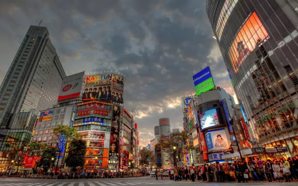 HD desktop wallpaper of a bustling man-made cityscape in Tokyo at dusk with illuminated billboards and crowds under a dramatic sky.