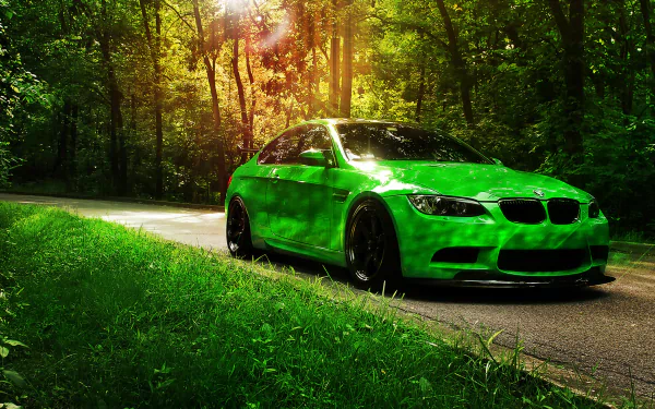 A striking green BMW car is parked on a serene forest road, basking in the warm light filtering through the trees. The image serves as an HD desktop wallpaper and background.