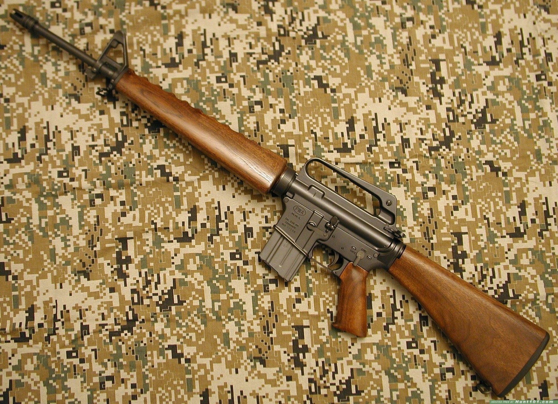 HD desktop wallpaper featuring a Colt AR-15 rifle with wooden stock and grip, displayed on a digital camouflage background.