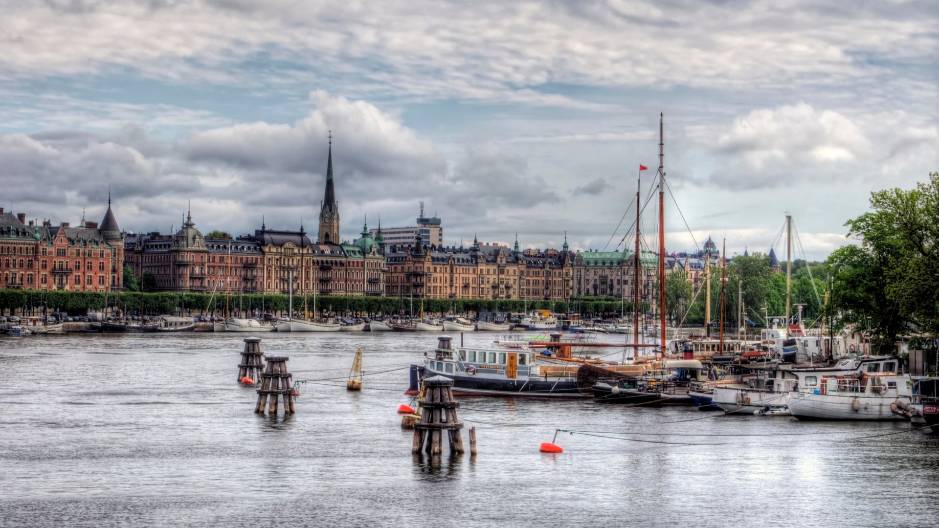 HD desktop wallpaper showing a man-made waterfront scene in Stockholm, Sweden with boats docked and historic city buildings under a cloudy sky.