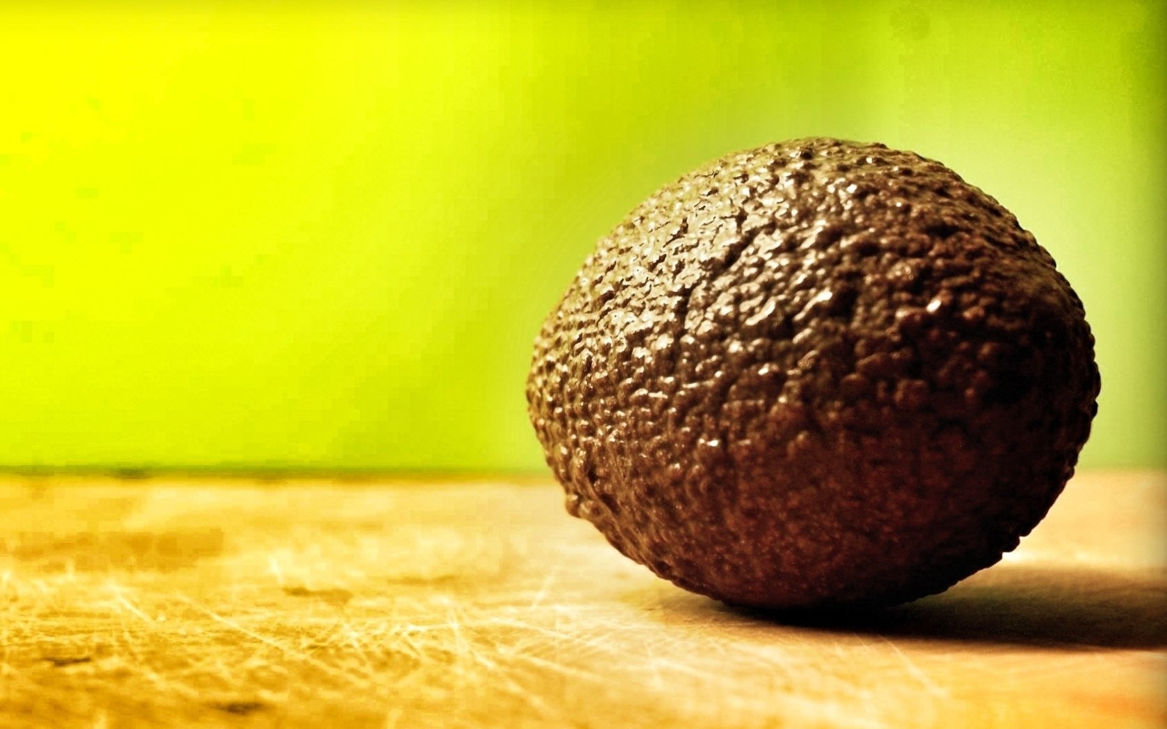HD desktop wallpaper featuring a single ripe avocado on a wooden surface with a bright green background, highlighting food and natural textures.