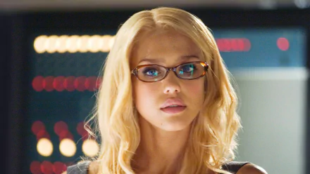 A close-up of Susan Storm from the movie Fantastic Four, featuring her blonde hair and glasses, set against a stylized background, capturing the essence of the character.