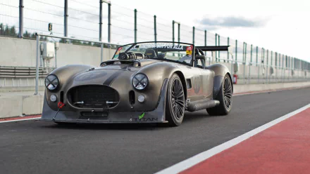 HD PC desktop wallpaper featuring a sleek AC Cobra vehicle parked on a racetrack with a modern, industrial backdrop.