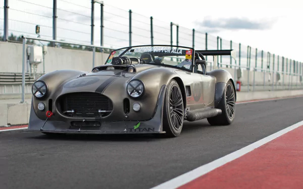 HD PC desktop wallpaper featuring a sleek AC Cobra vehicle parked on a racetrack with a modern, industrial backdrop.