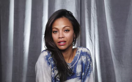 Zoe Saldana, an American actress, poses thoughtfully in front of a textured backdrop, showcasing her confident expression in this HD desktop wallpaper.