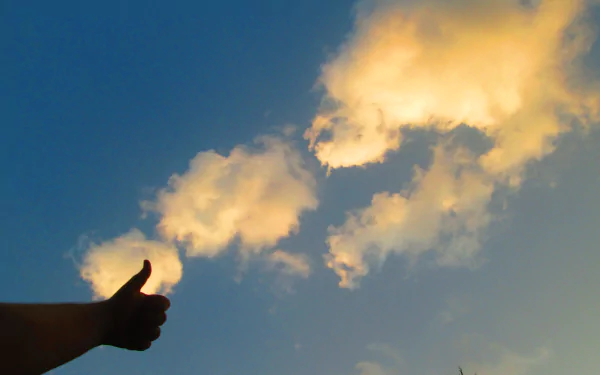 Silhouetted hand giving a thumbs-up toward glowing clouds in a deep blue sky — artistic 4K Ultra HD PC desktop wallpaper.