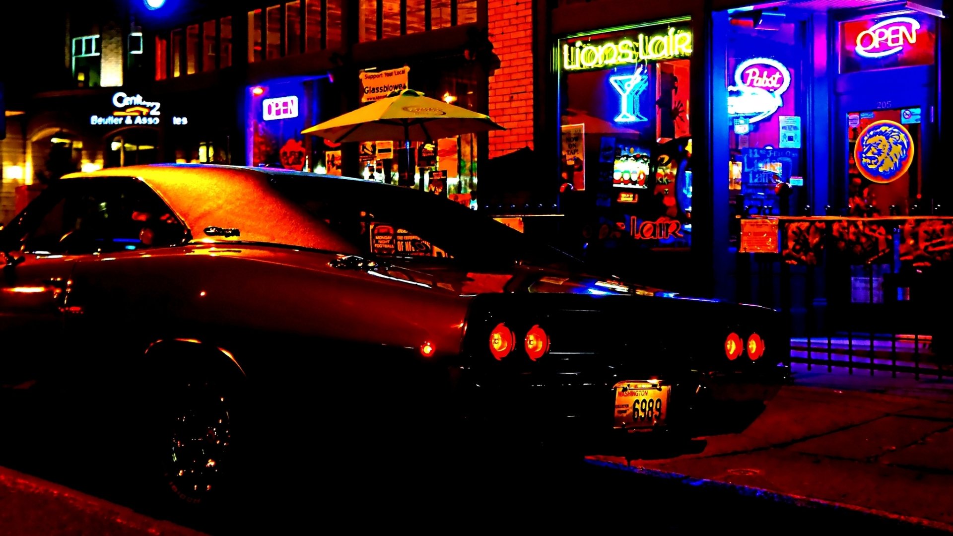 HD PC desktop wallpaper of a Dodge Charger parked under neon lights on a nighttime city street, rear view with glowing taillights and colorful storefront signs.
