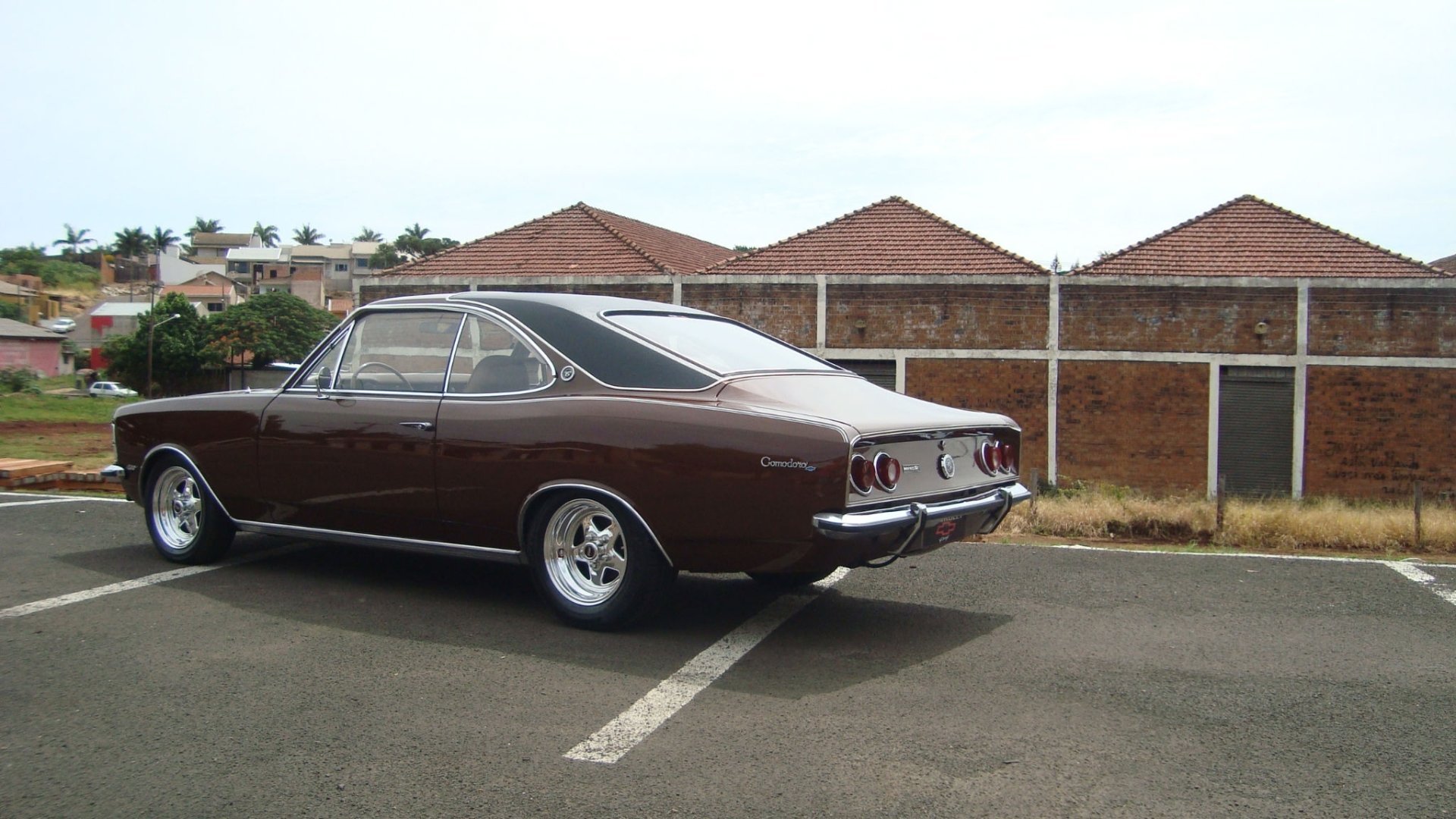 HD PC desktop wallpaper featuring a classic brown Chevrolet Opala Comodoro parked on an asphalt surface with buildings in the background.