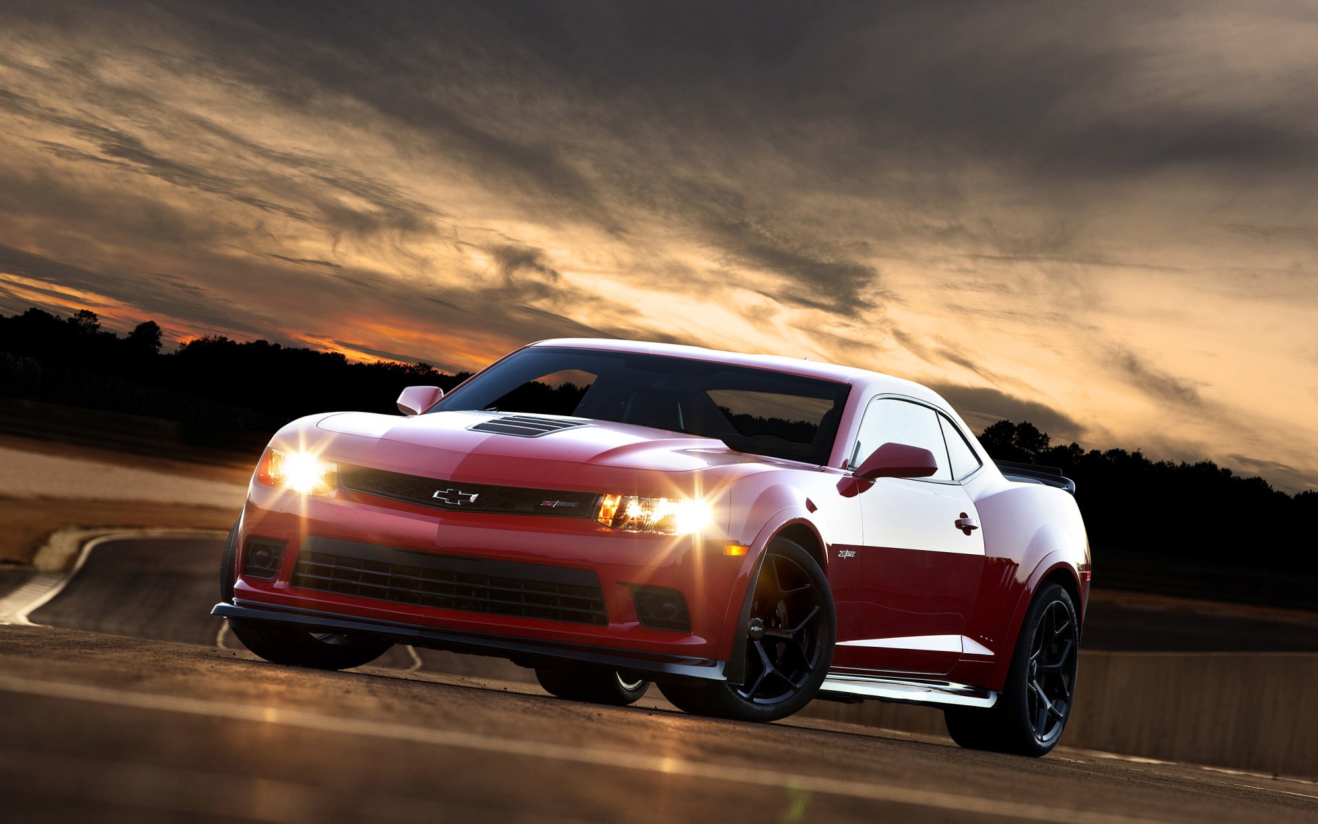 Red Chevrolet Camaro vehicle speeding on a dusk road under dramatic clouds — 2K Quad HD PC desktop wallpaper and background.