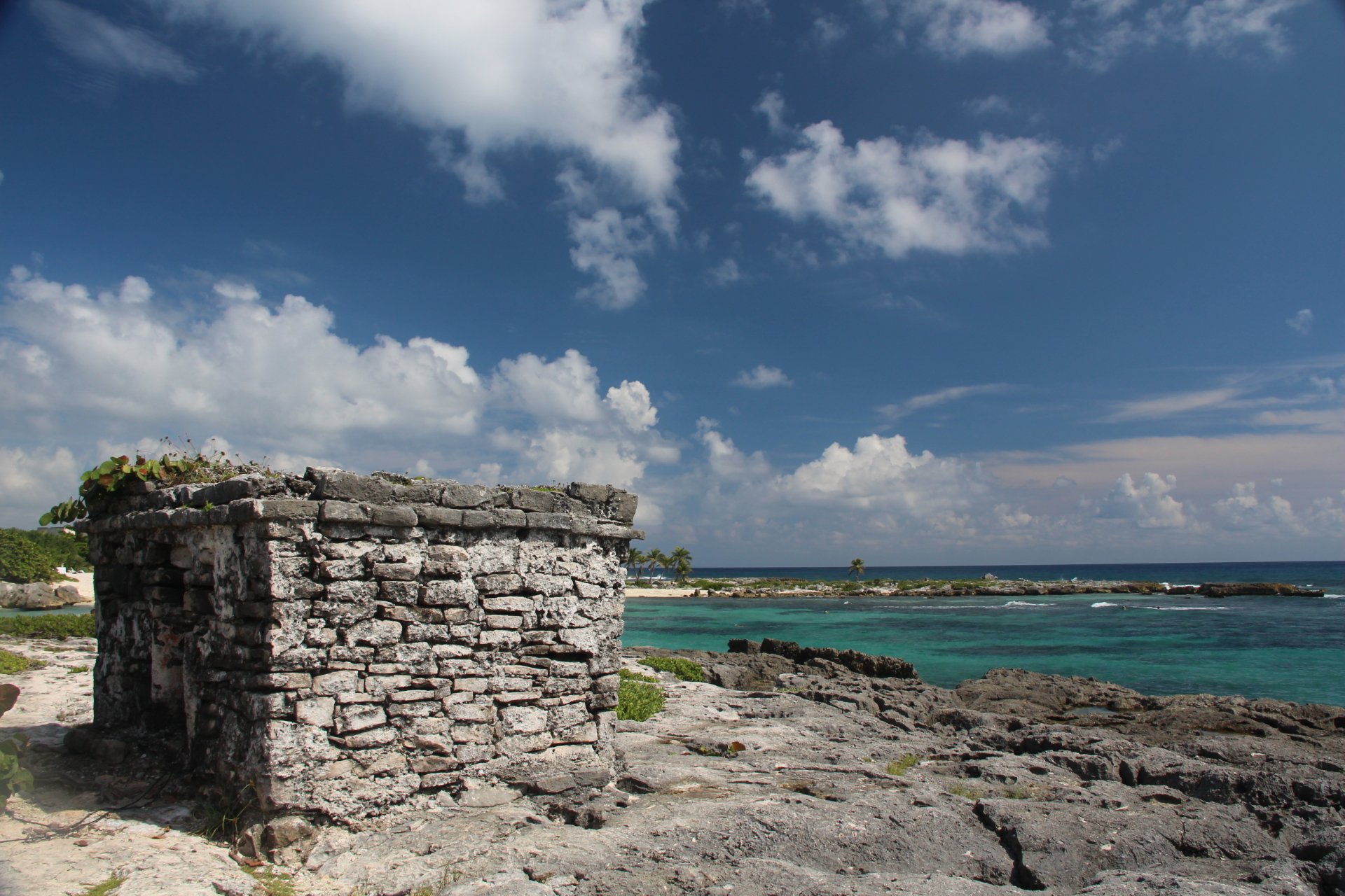 4K Ultra HD photo of a rocky beach in Tulum, Mexico, featuring ancient stone ruins under a partly cloudy sky with turquoise ocean waters.