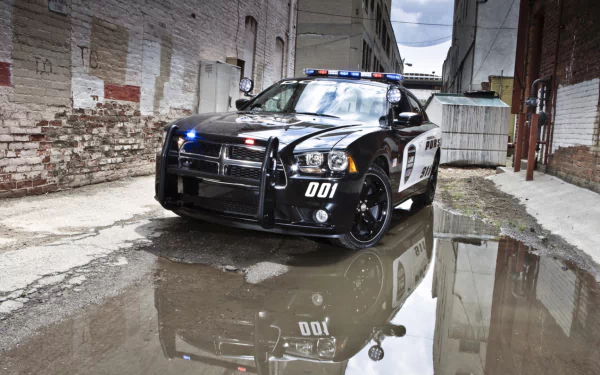 HD PC desktop wallpaper background: black Dodge Charger Pursuit police vehicle parked in an urban alley, reflected in a puddle.