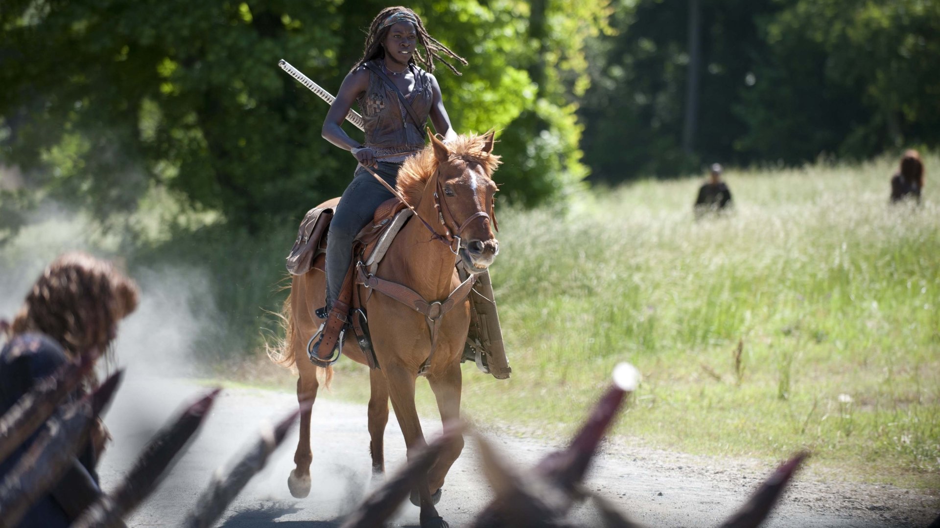 2K Quad HD wallpaper — dreadlocked woman on horseback, holding a katana as she rides down a sunlit road; cinematic TV drama scene from The Walking Dead.