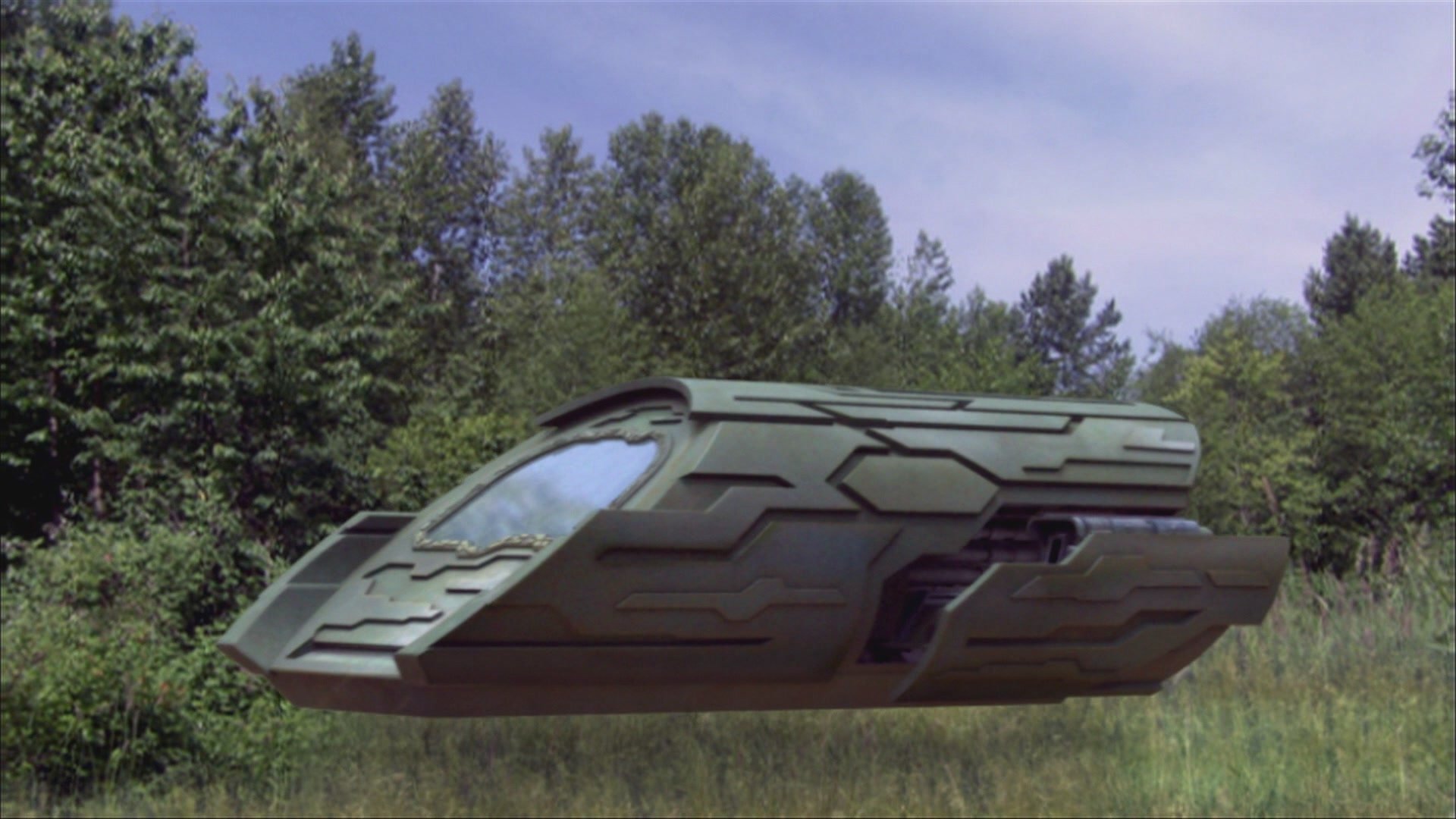 HD PC desktop wallpaper from the TV show Stargate Atlantis: a sleek gray Puddle Jumper shuttle hovering above a grassy clearing with trees under a blue sky.