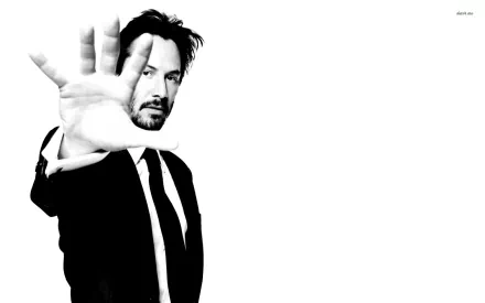 HD PC desktop wallpaper featuring celebrity Keanu Reeves in a black suit with his hand extended toward the camera against a white background.