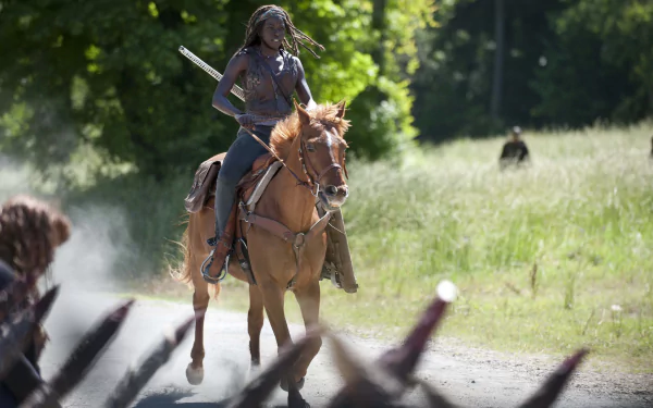 2K Quad HD wallpaper — dreadlocked woman on horseback, holding a katana as she rides down a sunlit road; cinematic TV drama scene from The Walking Dead.