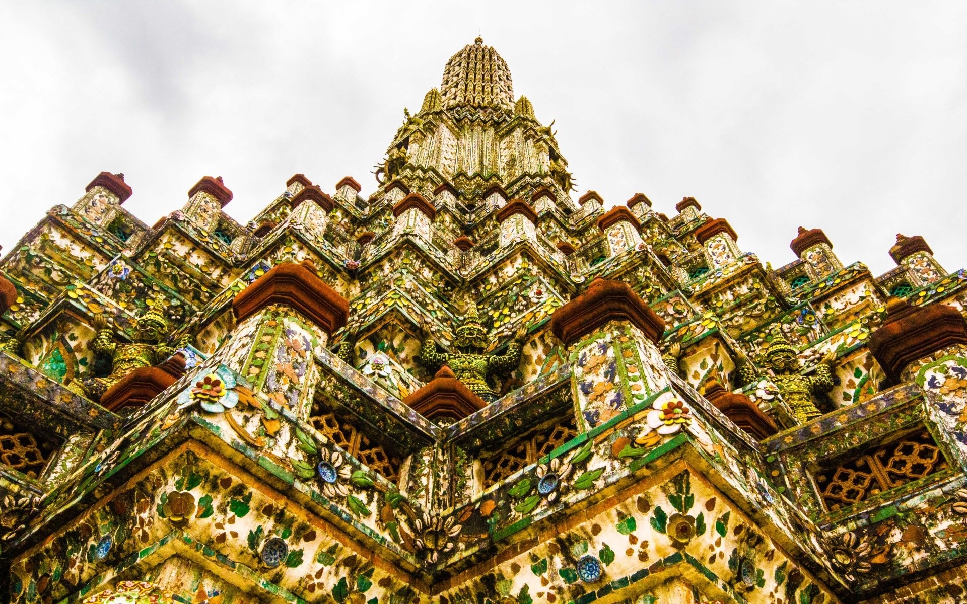Religious Wat Arun Temple spire in an HD PC desktop wallpaper, ornate porcelain mosaics and floral motifs rising toward a pale sky.