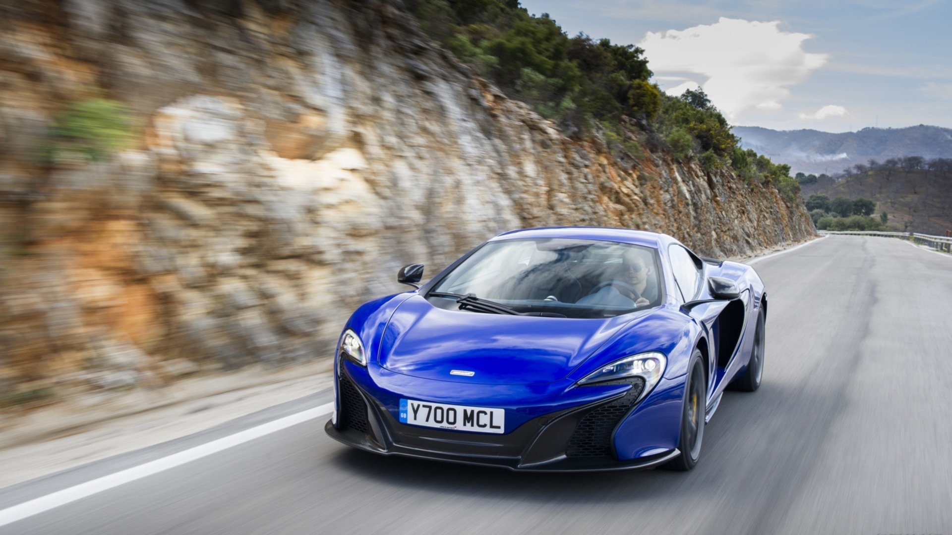 Blue McLaren 650S supercar driving along a winding coastal road — HD PC desktop wallpaper background.